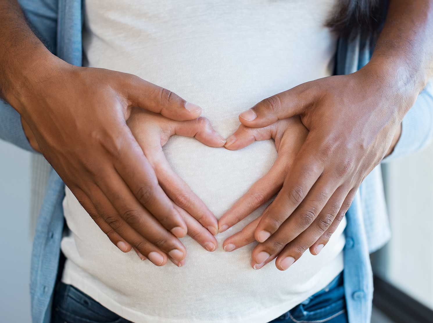 Couple making heart shape with hands on pregnant woman's belly