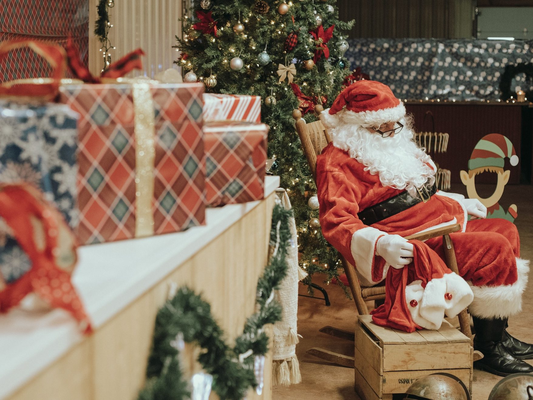 Presents in the foreground with Santa in background sitting rocking chair during breakfast with Santa