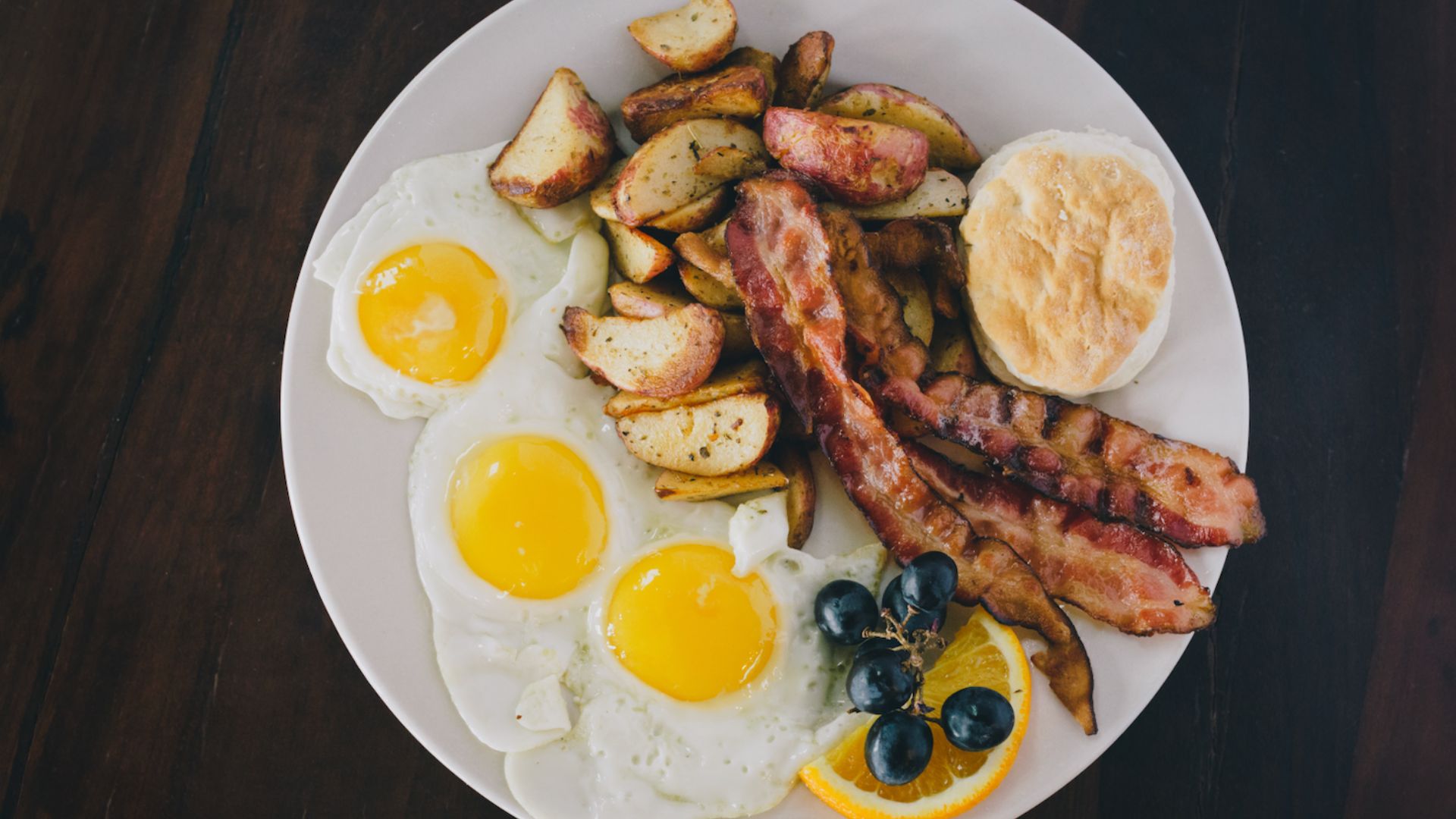 Holiday Brunch Plate with three fried eggs, roasted potatoes, bacon, blueberries, and an orange slice