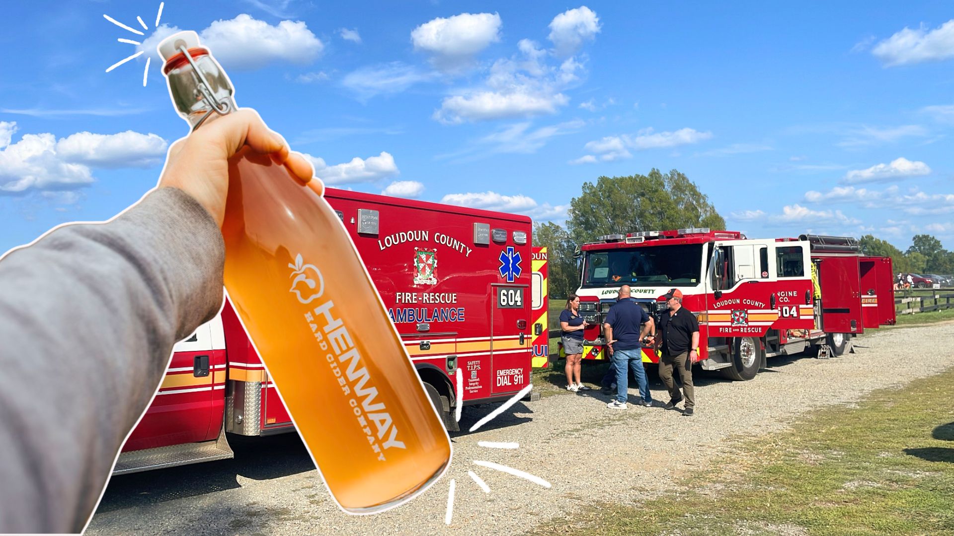 Hand holding Henway Hard Cider in front of fire trucks at Great Country Farm's First Responder Days